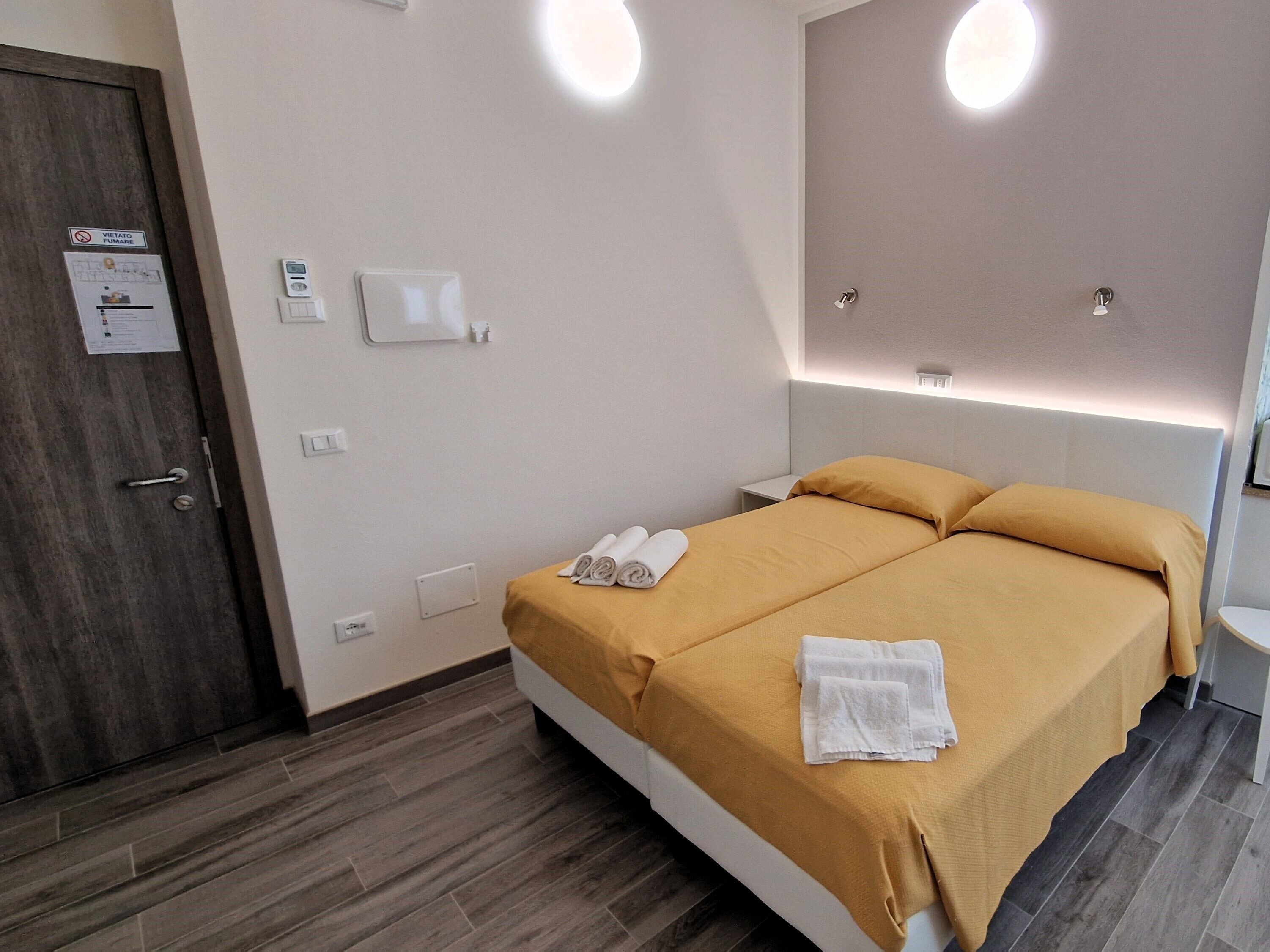 Une chambre d’hôtel comprenant un lit, une table de chevet, un thermostat fixé au mur et une porte avec une pancarte.