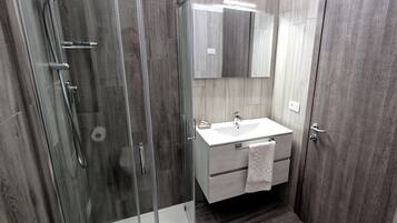 A modern bathroom with a glass-enclosed shower, a white sink, and a mirror above it.