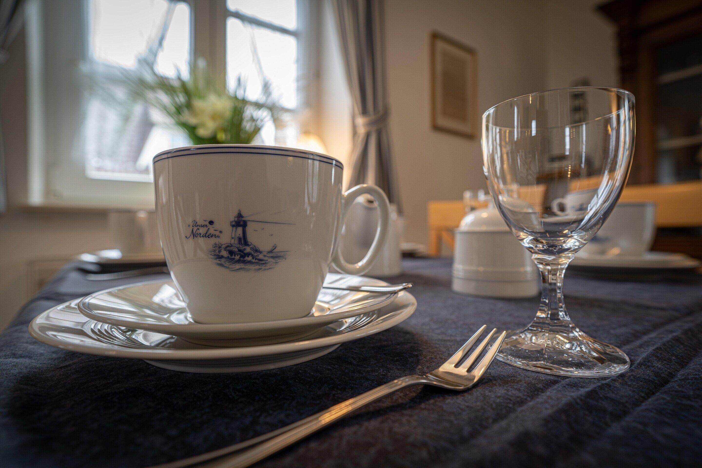 A table with a white cup and saucer with a blue design, a clear glass, and a fork.