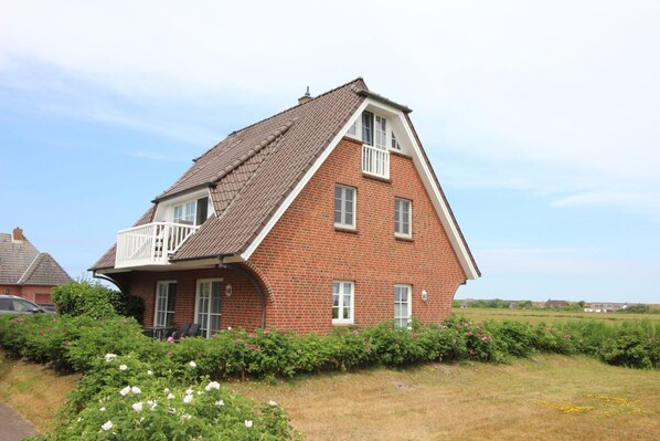 A red brick house with a sloped roof and a balcony. - Ferienwohnung in St. Peter-ording (St. Peter-Ording)