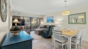 A modern hotel room with a balcony, a dining area, a sofa, and a TV.