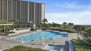 A hotel with a large building, a swimming pool area with two pools, and a covered seating area.