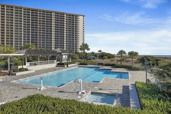 Un hotel con un edificio grande, un área de piscina con dos piscinas y una zona de estar cubierta.