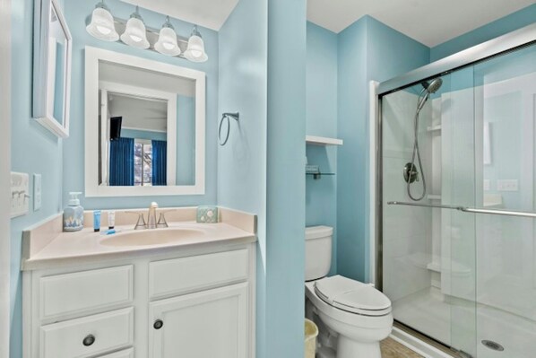 A bathroom with a white vanity, a mirror, a toilet, and a glass-enclosed shower.