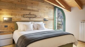 A bedroom with a wooden headboard, a bed with white bedding, two wall-mounted lights, and a window with a green frame.