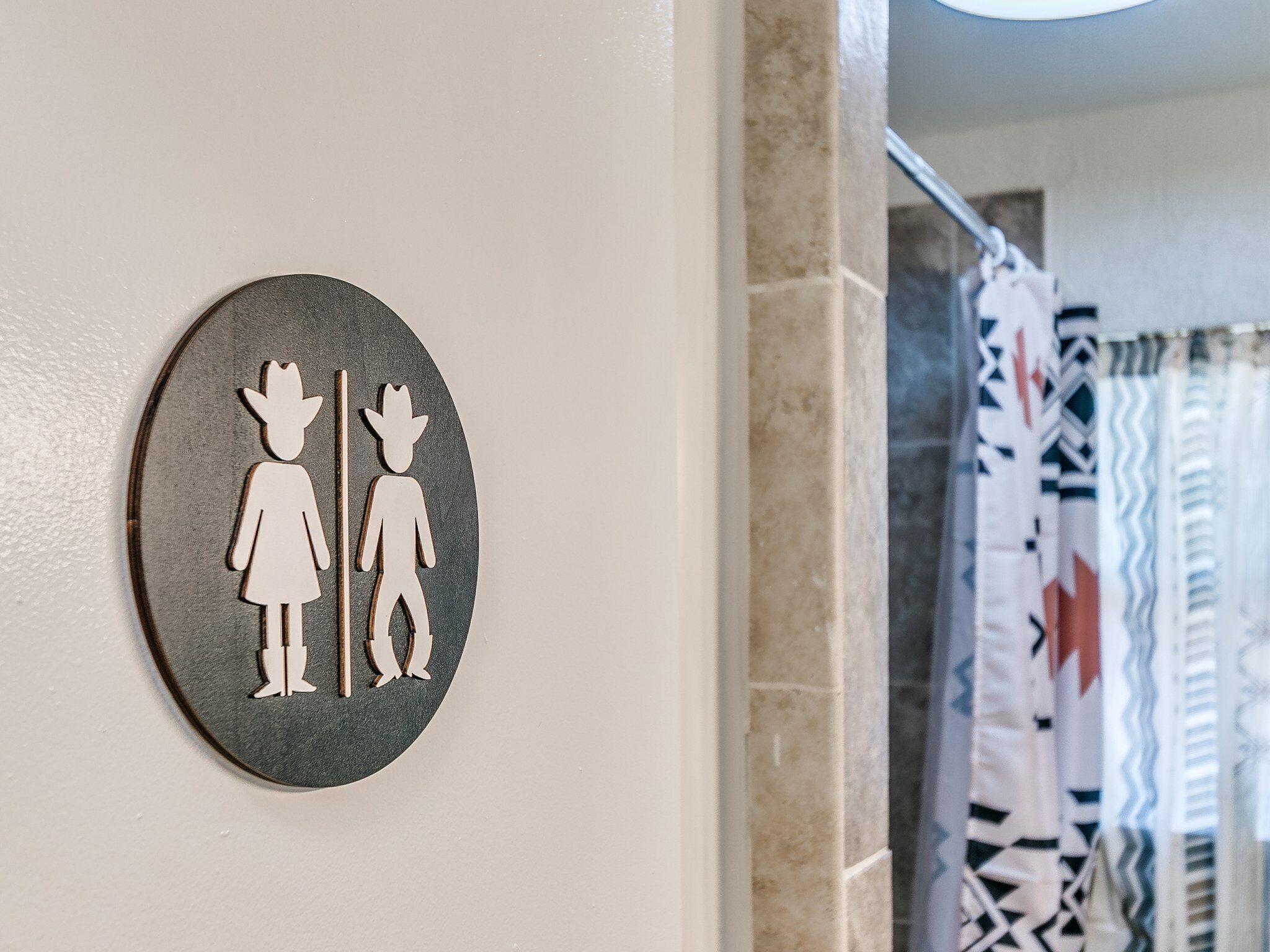 Ein rundes Schild mit zwei Personen, eine mit Hut und eine ohne, zur Kennzeichnung von WC für Damen und Herren.