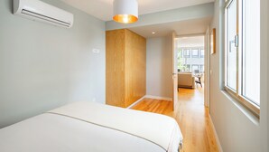 Ein modernes Schlafzimmer mit einem Bett, einer Klimaanlage, einem Holzschrank und Blick durch ein Fenster.