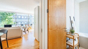 Ein modernes Interieur mit einer Holztür, einem weißen Sofa, einem Essbereich und Blick auf ein Gebäude.