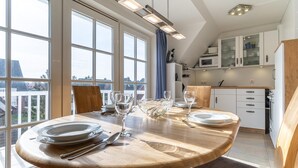 Zona pranzo con tavolo rotondo apparecchiato per quattro persone, ampie finestre e cucina con mobili bianchi e forno a microonde.