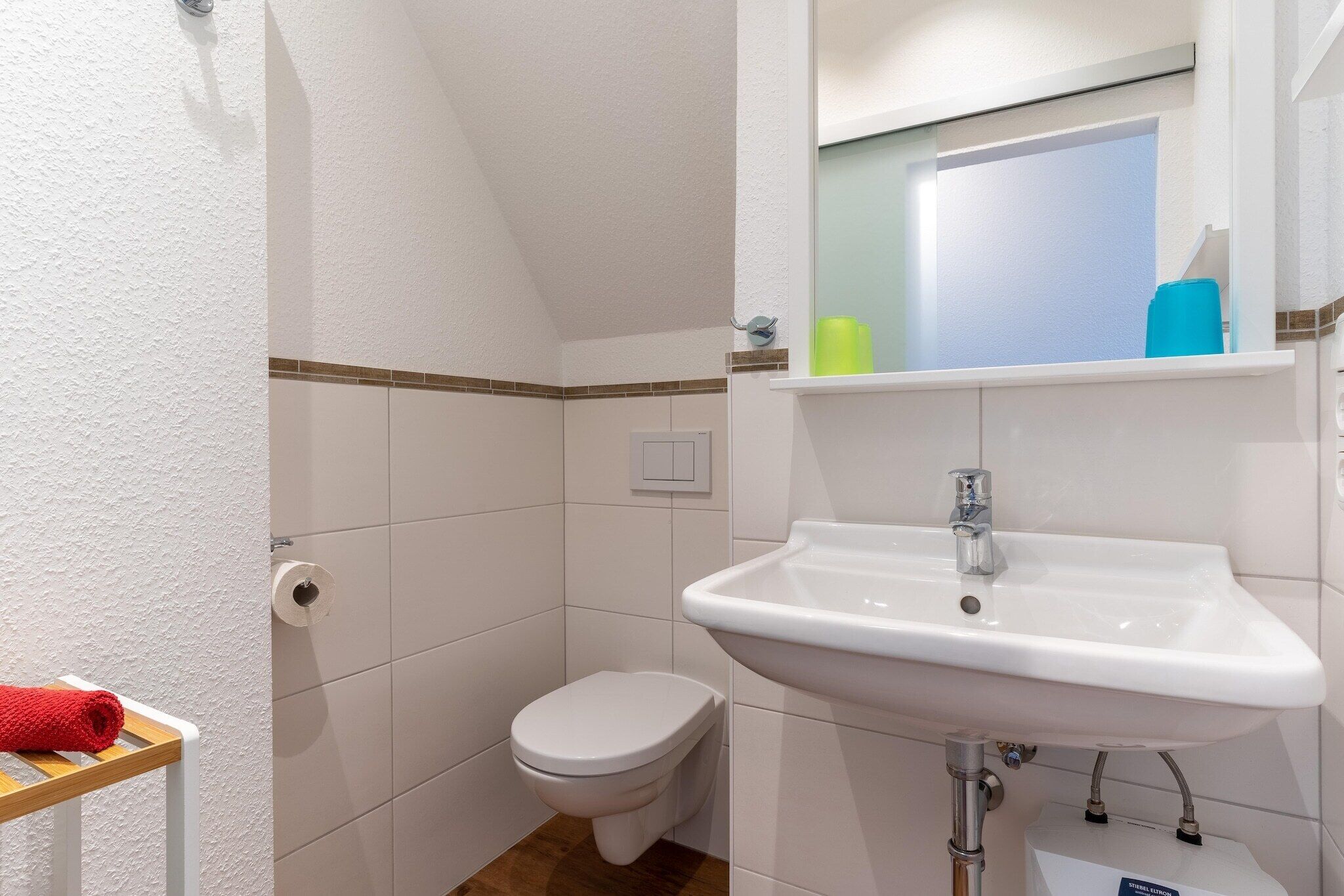 Un baño con inodoro blanco, lavamanos y espejo sobre él.