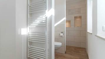 A modern bathroom with a toilet, a towel rack, and a wooden floor.