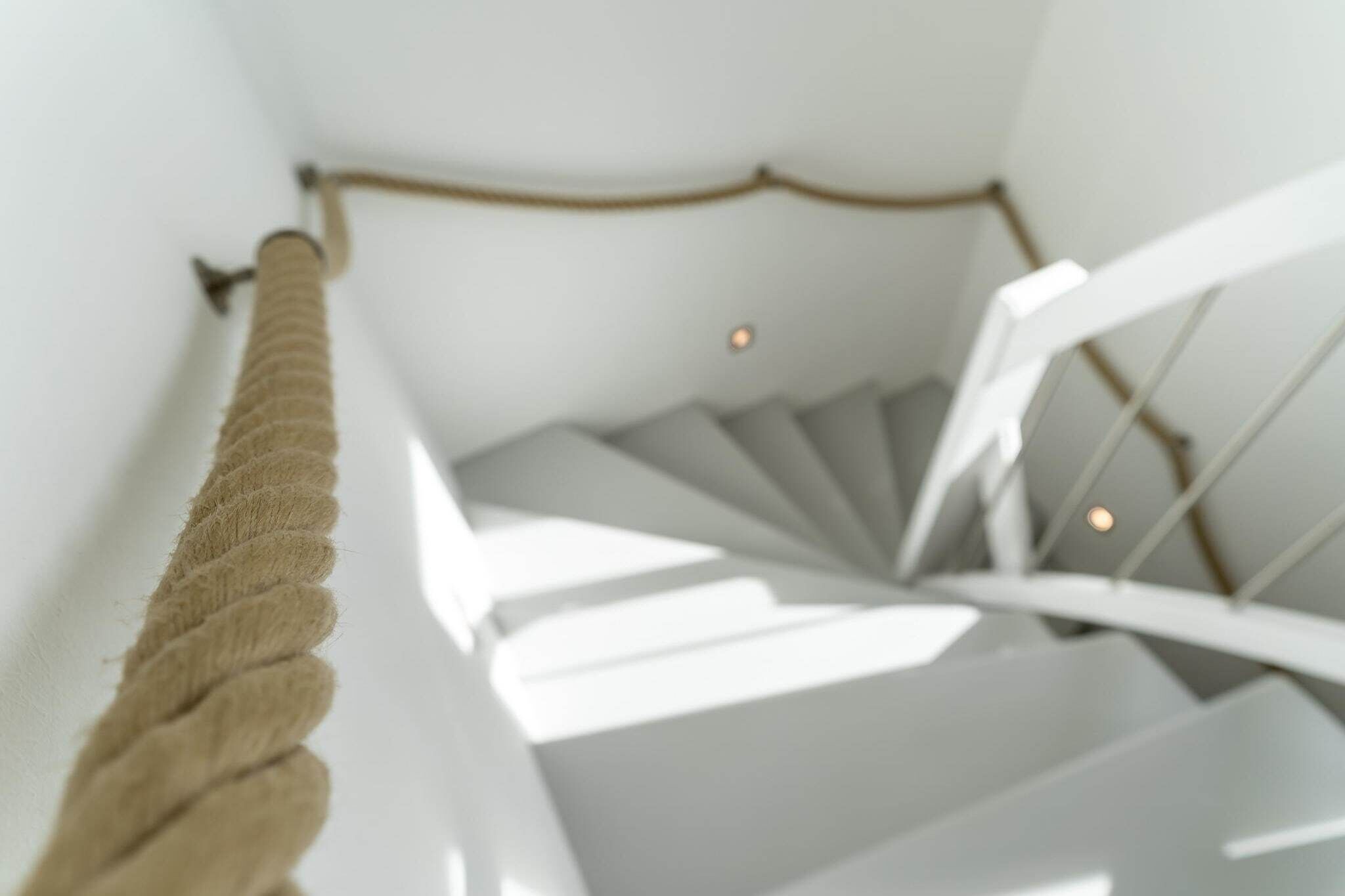 Eine Wendeltreppe mit Seilgeländer, weißen Wänden und einer Deckenleuchte.