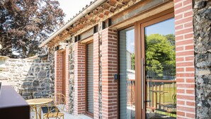 A building with a stone wall, a brick facade, and a glass door leading to an outdoor seating area. - Our establishment is located not far from Clermont-Ferrand in the charming littl (Saint-Saturnin)