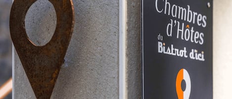 A sign with the text 'Les Chambres d'Hotes du Bistrot d'Ici' and a location pin icon.