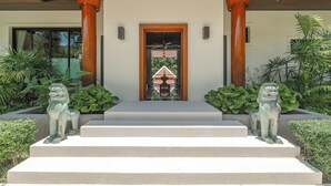 A building entrance with a wooden door, a ceiling fan, and two lion statues on the steps. - Naiharn 4br Private PoolVilla near Beach (Rawai)