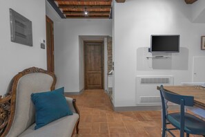 Una habitación acogedora con una mesa de comedor de madera, una silla azul y un sofá con un cojín verde azulado. Un televisor está montado en la pared sobre la mesa.
