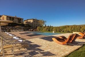 A poolside area with lounge chairs, a swimming pool, and stone buildings in the background. -  Le Torri, Borgo Campassini, Monteriggioni (Monteriggioni)