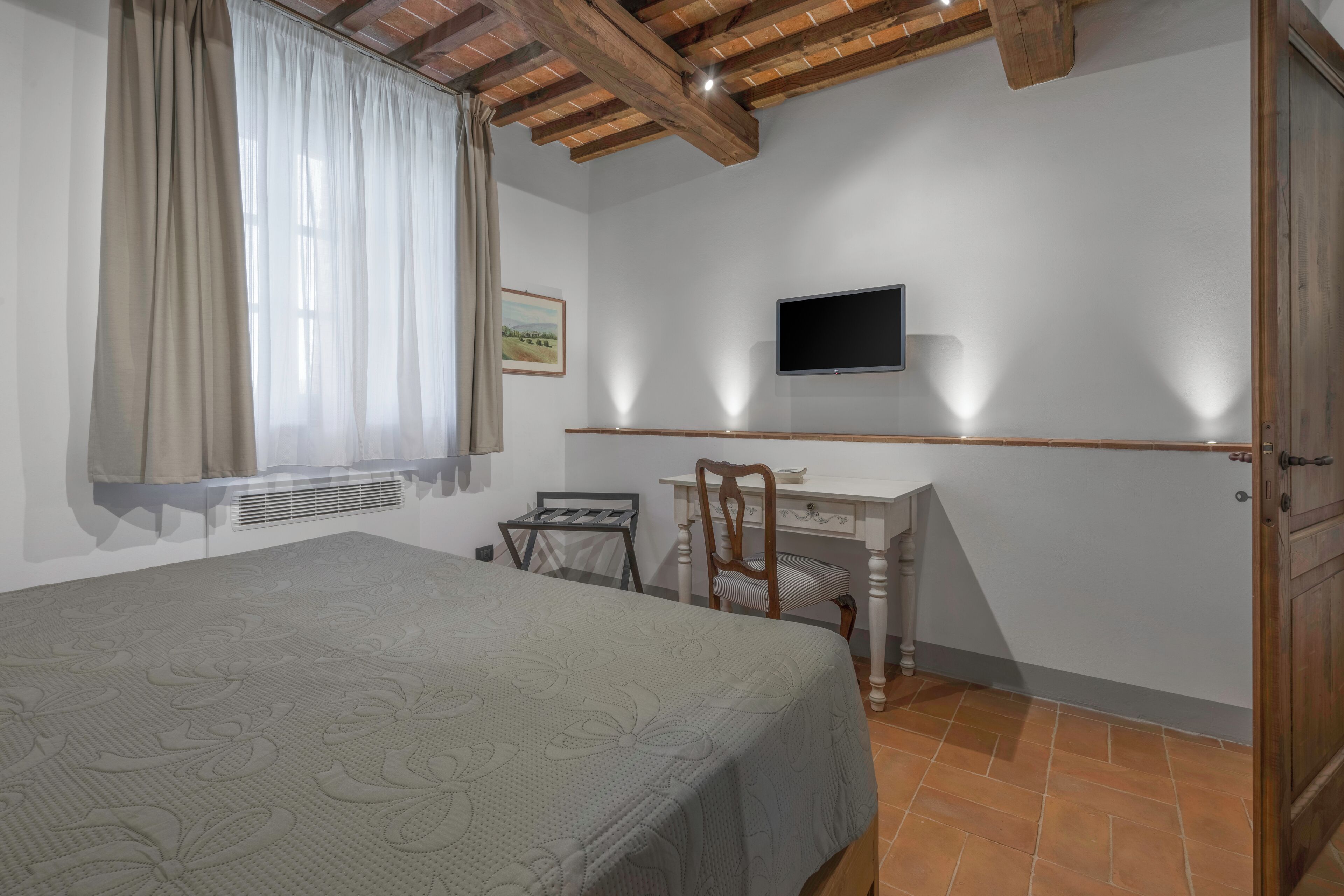 A bedroom with a bed, a desk, a chair, a TV, and a window with curtains.