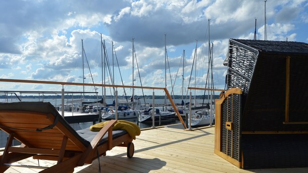 A wooden deck with a lounge chair and a small cabin. - Houseboat Hecht with spacious roof terrace in Schleswig (Schleswig)