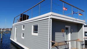 A docked houseboat with a balcony, windows, and a flag. - Houseboat Hecht with spacious roof terrace in Schleswig (Schleswig)