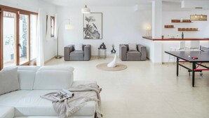 Een moderne woonkamer met een witte bank, grijze fauteuils, een salontafel en een eethoek met een tafel en stoelen.