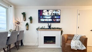 A modern living room with a fireplace, a mounted TV displaying various channels, and a cozy seating area. - Lux 1BR Ski IN/OUT: King+Queen, No Sleeper! @Lift (Snowshoe)