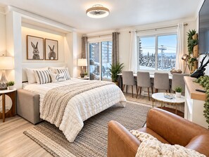 Een moderne hotelkamer met een groot bed, een zithoek met stoelen, een eettafel en uitzicht op een besneeerd landschap.