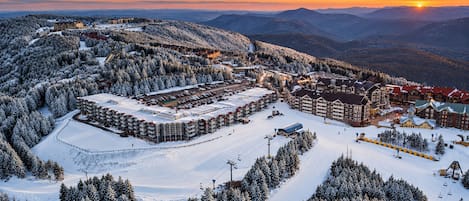 A snow-covered resort with multiple buildings, a ski slope, and a mountain backdrop.