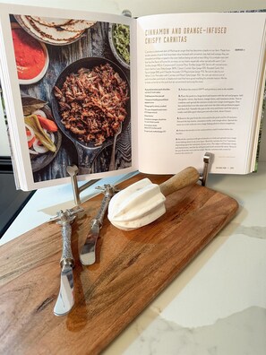 A cookbook open to a recipe page with a wooden cutting board, a rolling pin, and a knife.
