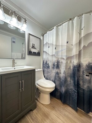 Een badkamer met toilet, wastafel, kastje, spiegel en een douchegordijn met een bosmotief.