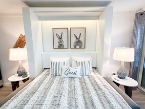 Een netjes ingerichte slaapkamer met een groot bed, twee ingelijste afbeeldingen van konijnen aan de muur, en twee bedlampen.