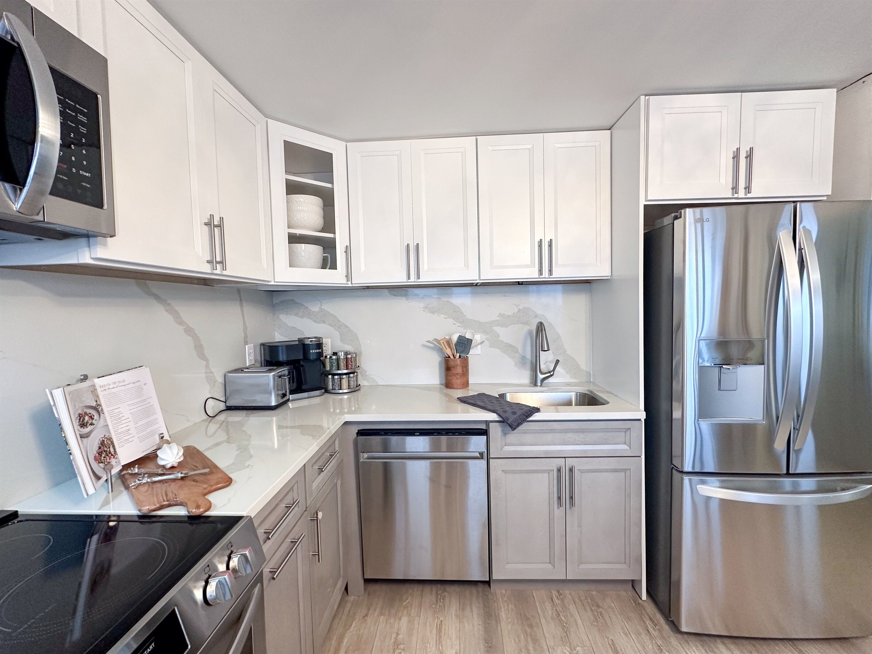 A modern kitchen with white cabinets, stainless steel appliances, a microwave, a dishwasher, and a refrigerator.