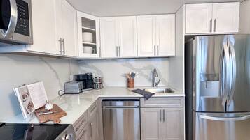 A modern kitchen with white cabinets, stainless steel appliances, a microwave, a dishwasher, and a refrigerator.