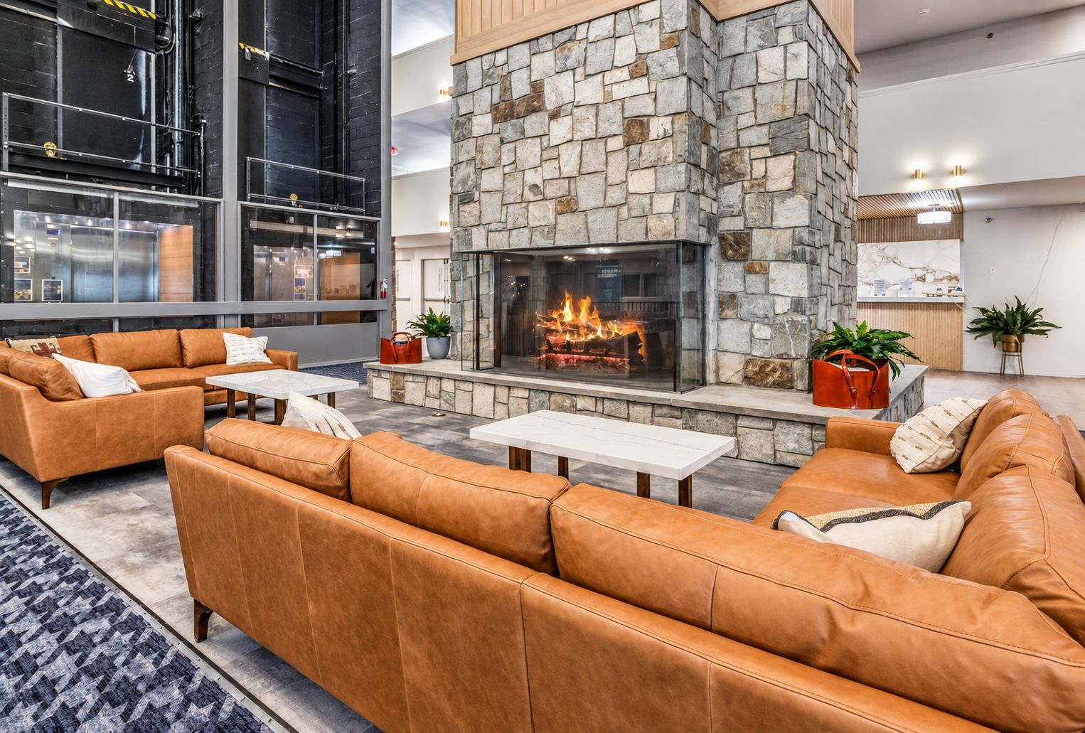 A modern lounge area with leather sofas, a stone fireplace, and a glass partition.