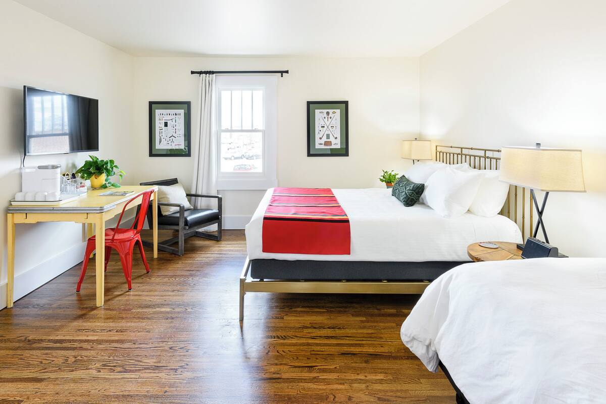 Une chambre d’hôtel avec un lit, un bureau et une chaise, une télévision et deux tableaux encadrés au mur.