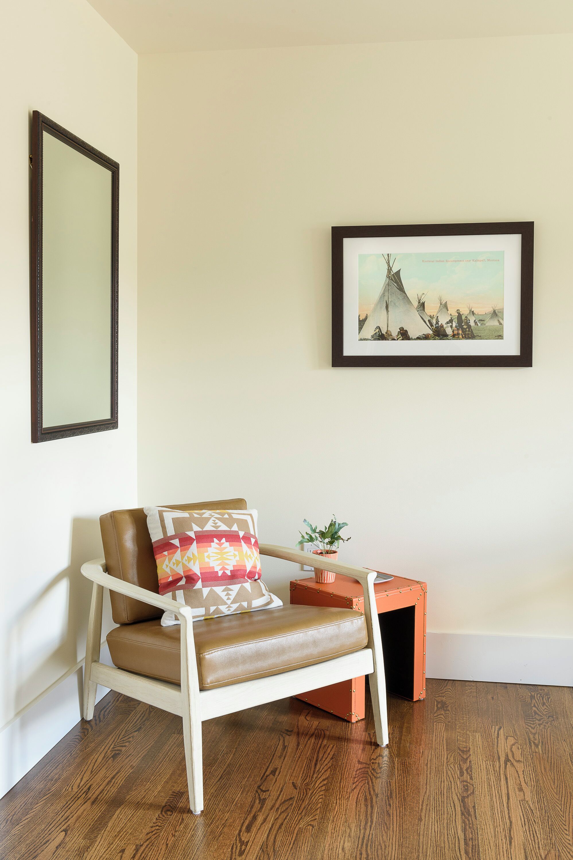 A chair with a cushion, a framed picture on the wall, and a small table with a plant.