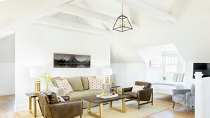 A spacious living room with a high ceiling, a central coffee table, a sofa, and two armchairs. A painting is on the wall, and a TV is mounted on the wall. - Sherman Lodge (Kalispell)