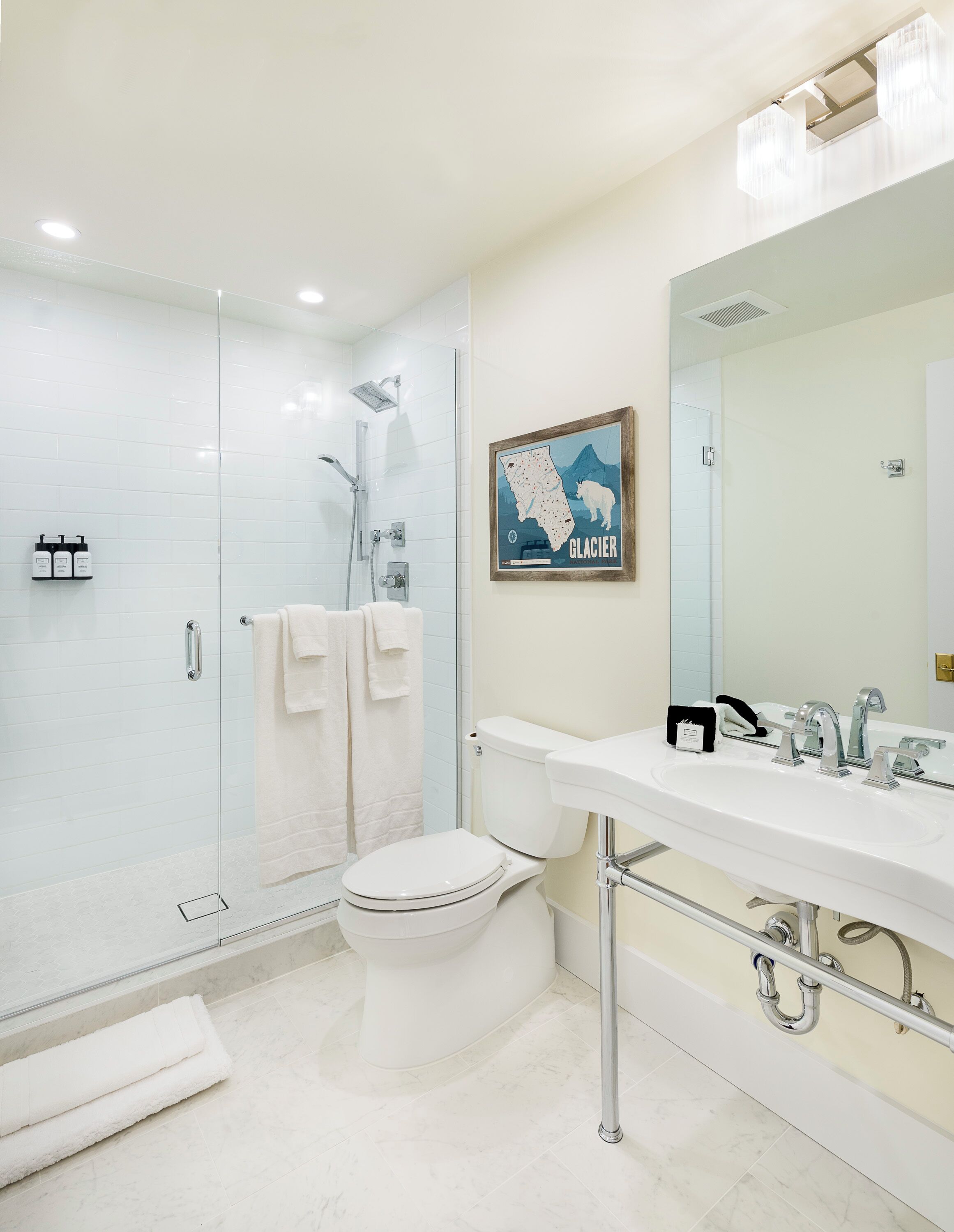 A modern bathroom with a glass-enclosed shower, a toilet, a sink with a mirror, and a framed map on the wall.