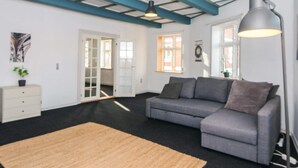 A modern living room with a grey sofa, a wooden rug, and a large floor lamp. - 4 Person Holiday Home in Ringkobing (Ringkobing)