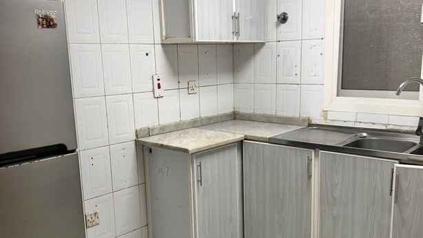 Cozinha compacta com armários brancos, pia de aço inoxidável e geladeira.