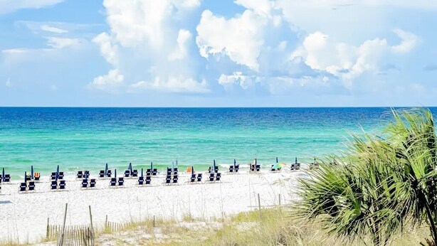 Ein Strand mit Reihen von Liegestühlen und Sonnenschirmen, bewölkter Himmel und ruhiges Meer.