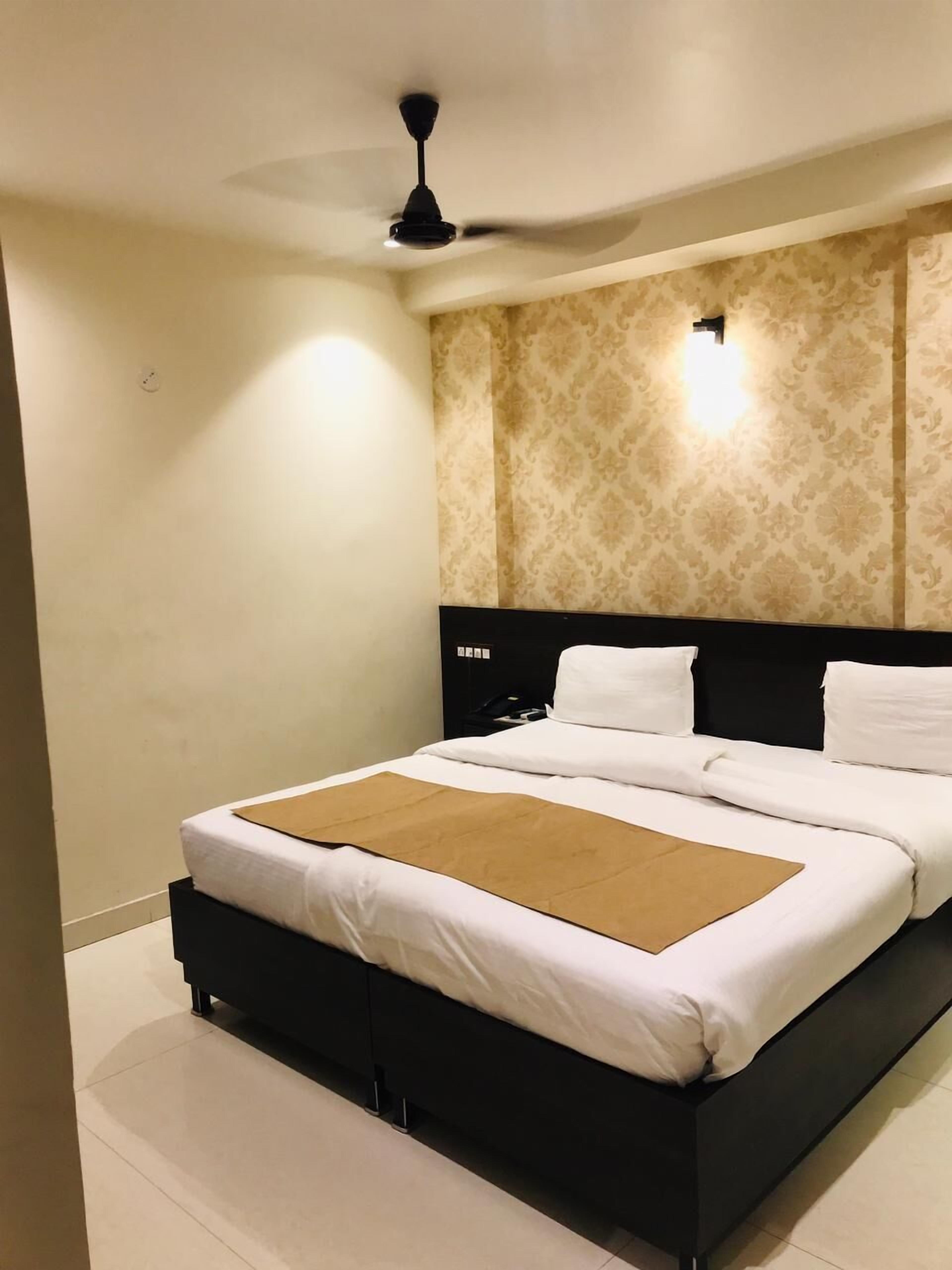 A modern hotel room with a large bed, a ceiling fan, and a patterned wallpaper.