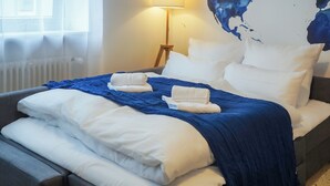 A neatly made bed with white and blue bedding, a world map on the wall, and a standing floor lamp. - 7Seas Apartment mit Balkon (Kaiserslautern)