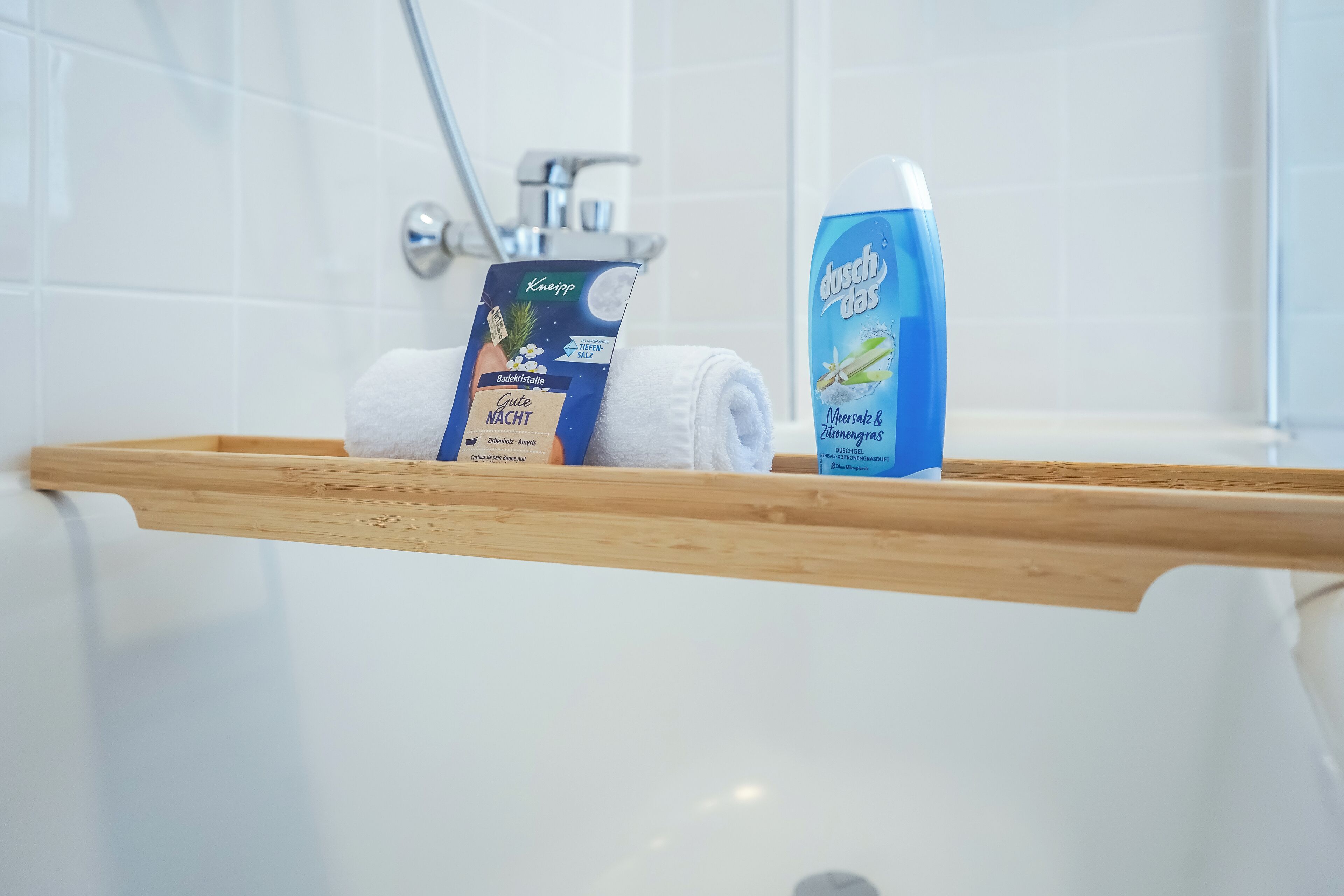 A bathroom with a wooden shelf holding a towel, a box of Kiepert soap, and a bottle of Dusch-Tas shower gel.
