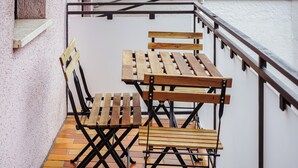 A balcony with a wooden table and chairs, a metal railing, and a white wall. - 7Seas Apartment mit Balkon (Kaiserslautern)
