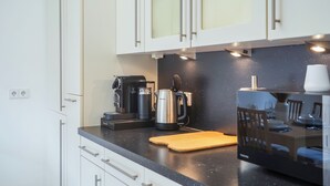 A modern kitchen with white cabinets, a black countertop, a coffee maker, a kettle, and a microwave. - 7Seas Apartment mit Balkon (Kaiserslautern)