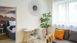 A modern living room with a bed, a desk, a sofa, a large wall clock, and a window with sheer curtains. - 7Seas Apartment mit Balkon (Kaiserslautern)