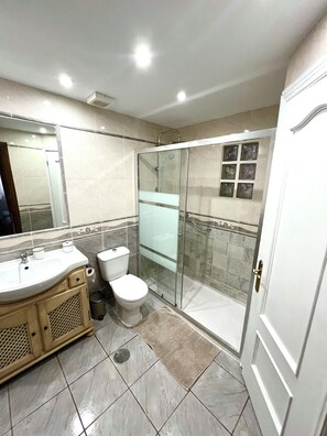 Un baño moderno con ducha envuelta en vidrio, lavamanos con espejo e inodoro.