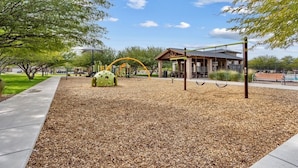 A playground with a climbing structure, swings, and a covered seating area.