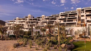 A modern resort with multi-story buildings, a landscaped garden with cacti and palm trees, and a pool area. - Whales & Waves from Your Terrace • Oceanfront 2BR (Los Cerritos)